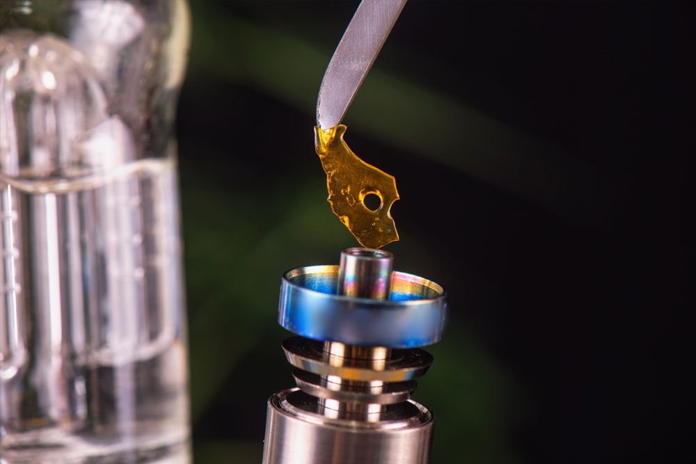 Macro detail of dabbing tool with small piece of cannabis oil - shatter suspended over a metal rig - medical marijuana concentrates concept