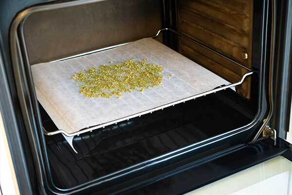 cannabis buds ground up and spread out on a baking sheet in an oven