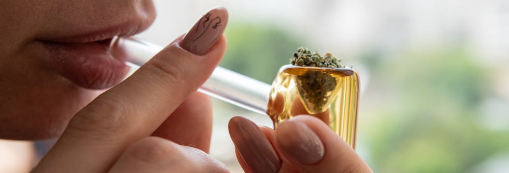 Cannabis bud in glass pipe being held next to mouth