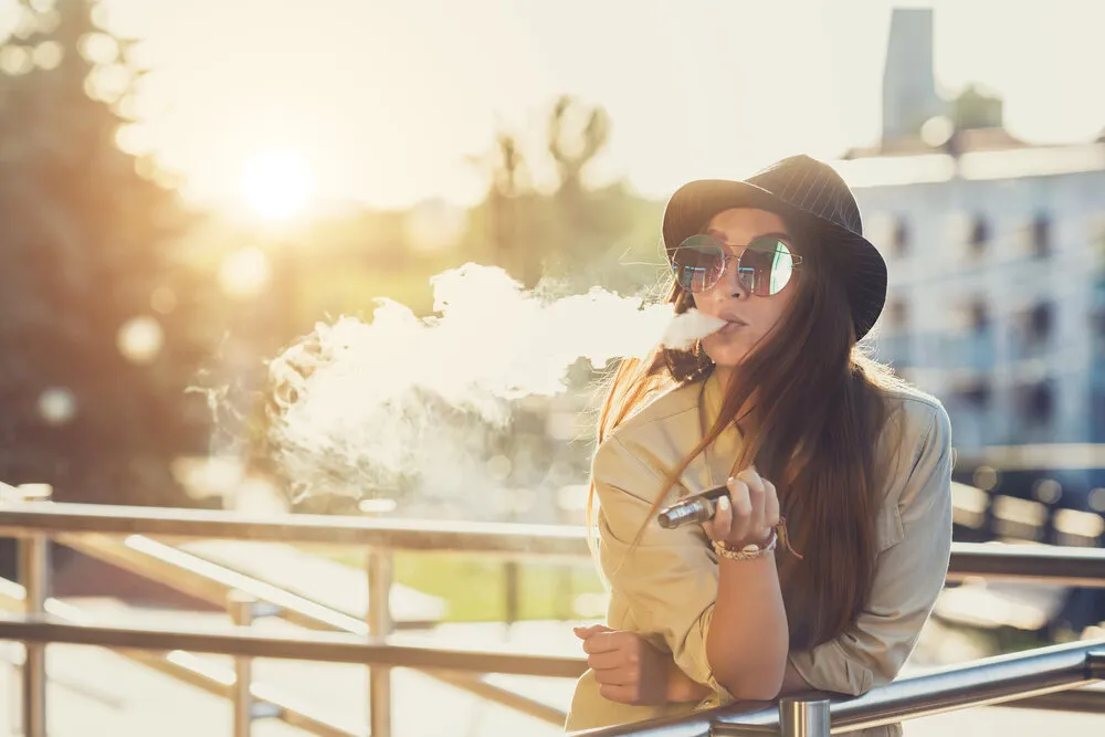 a woman with sunglasses smoking a thc vape leaning over a metal pole